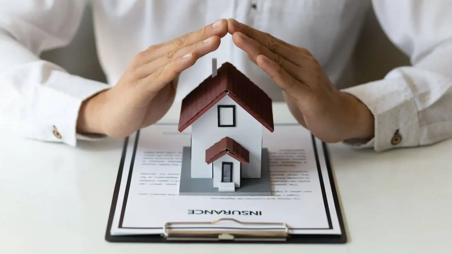 Person reviewing Geico home insurance policy details on a tablet, with a home in the background.