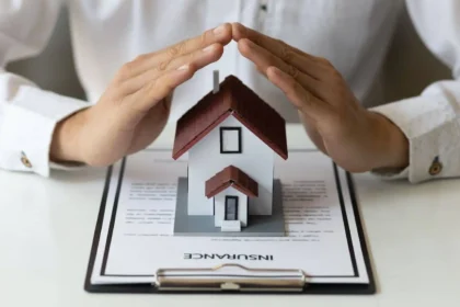 Person reviewing Geico home insurance policy details on a tablet, with a home in the background.